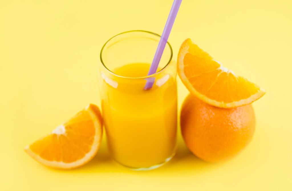 A Glass of Orange Juice with Orange Slices on a Yellow Background